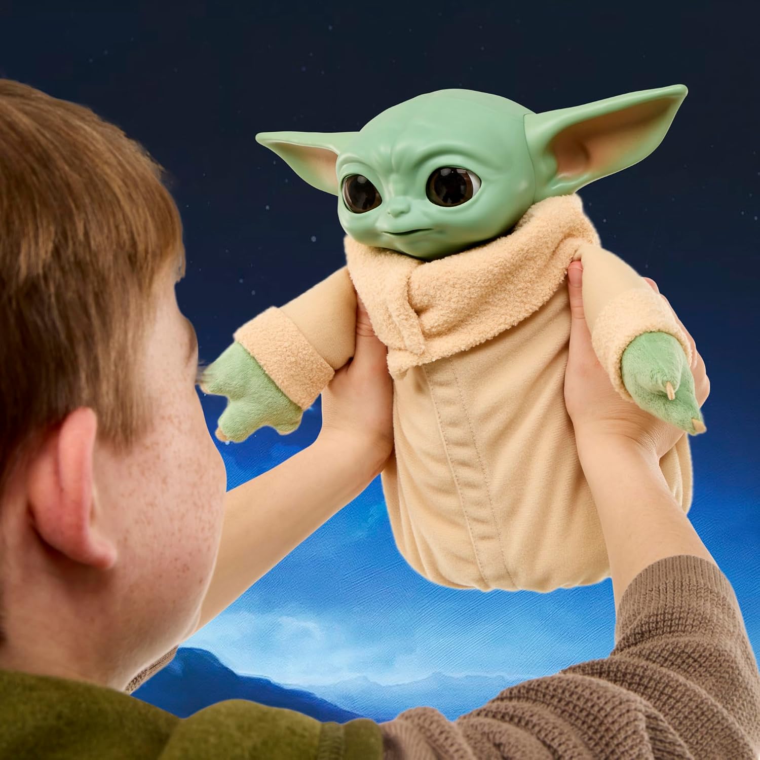 A child holding the Star Wars Action Buddy Grogu animatronic plush up in front of them